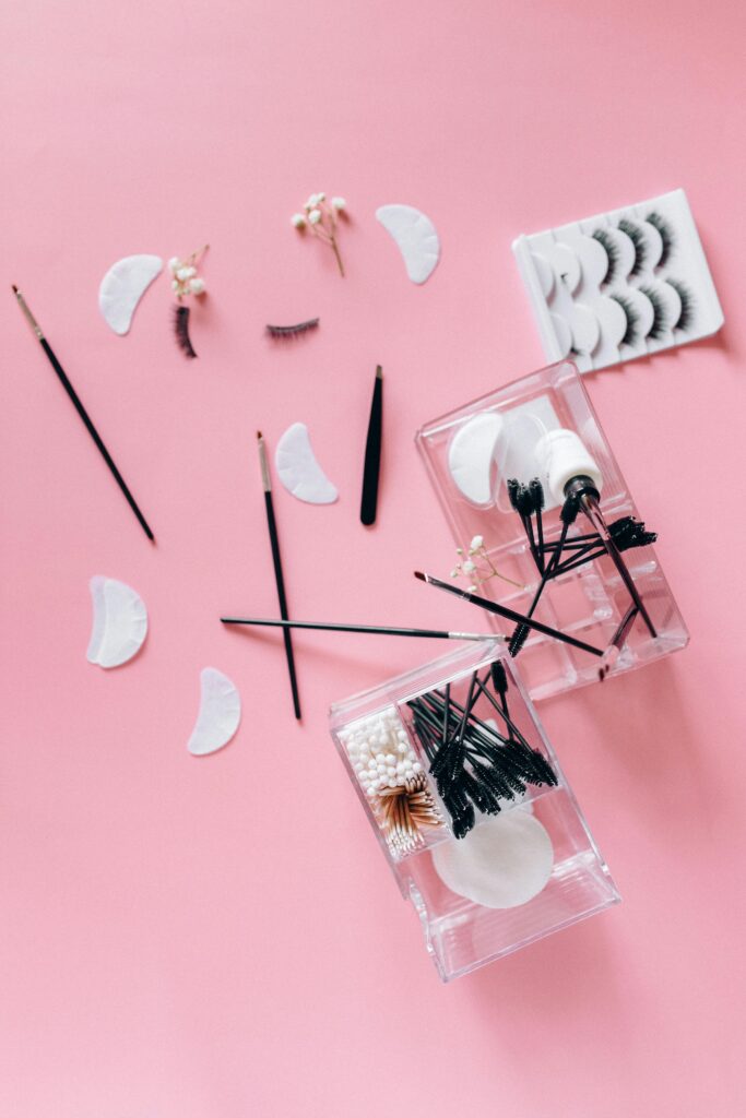 Flat lay of makeup tools and accessories on a pink background, ideal for beauty projects.